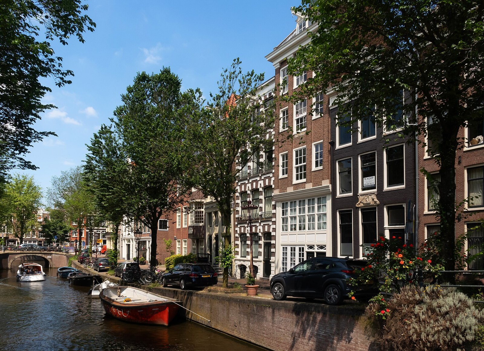 Eine Gracht mit Booten, Bäumen und Backsteinhäusern an einem sonnigen Tag