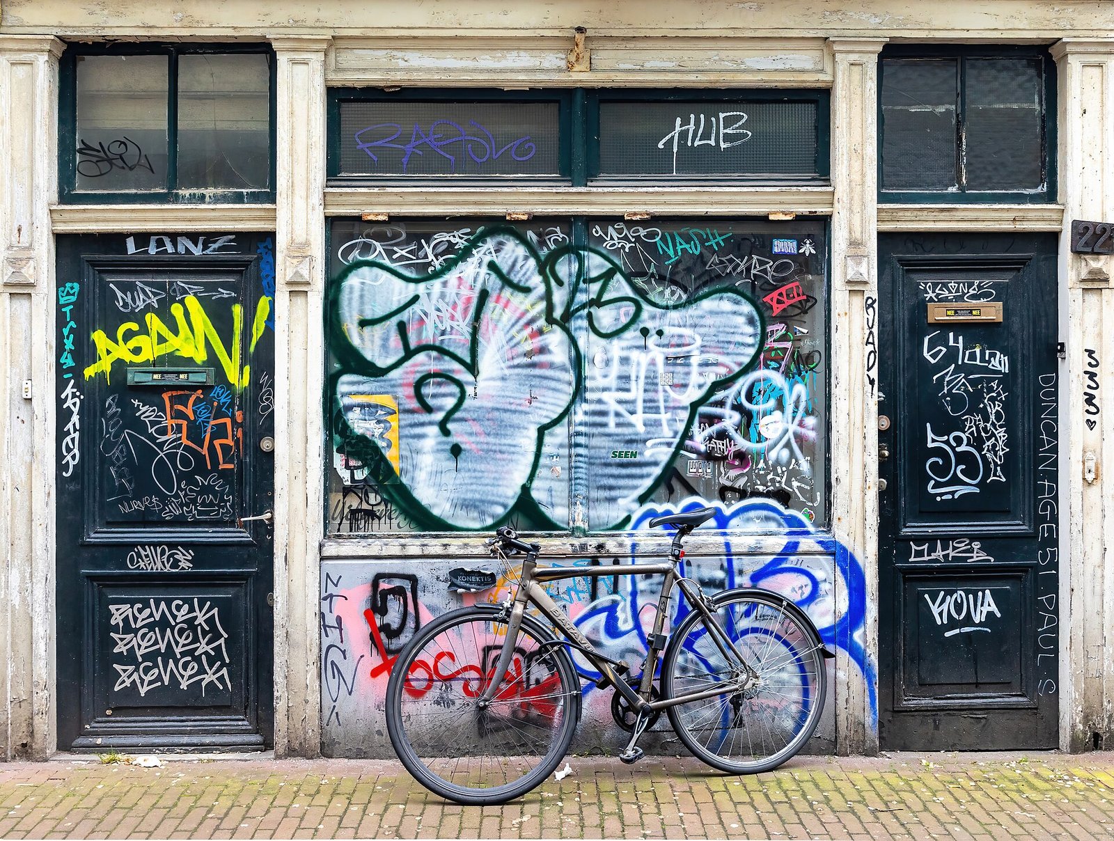 Ein an eine mit Graffiti bedeckte Hauswand gelehntes Fahrrad zwischen zwei dunklen Türen