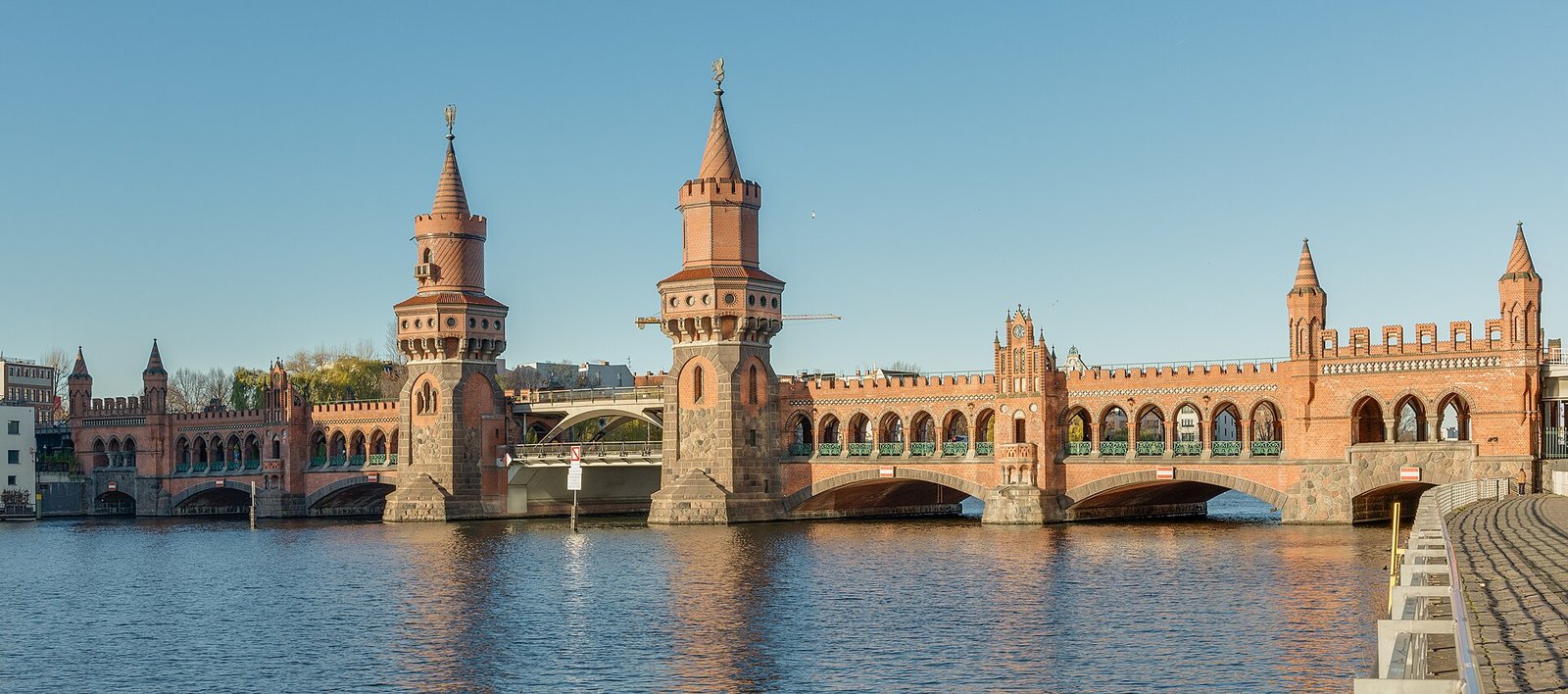 Die Oberbaumbrücke aus rotem Backstein mit zwei Türmen über der Spree unter blauem Himmel