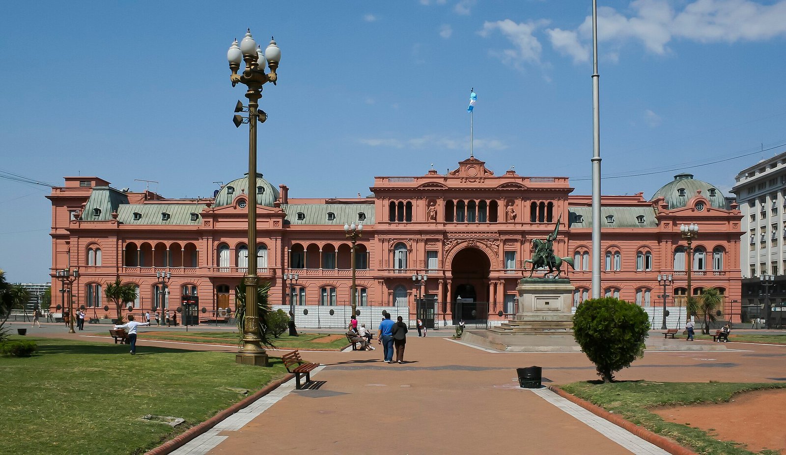 Die rosafarbene Casa Rosada an der Plaza de Mayo unter blauem Himmel, davor Laternen und ein Reiterdenkmal