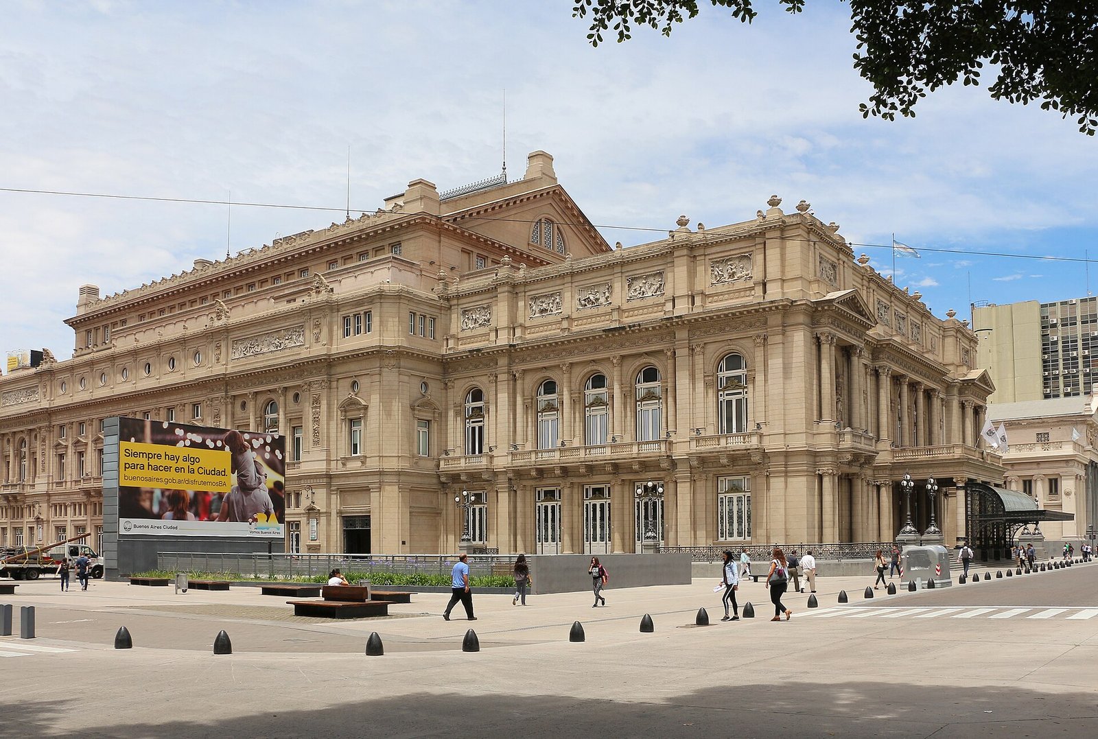 Die Seitenfassade des Teatro Colón mit Säulen und Reliefs, davor Passanten auf dem Platz