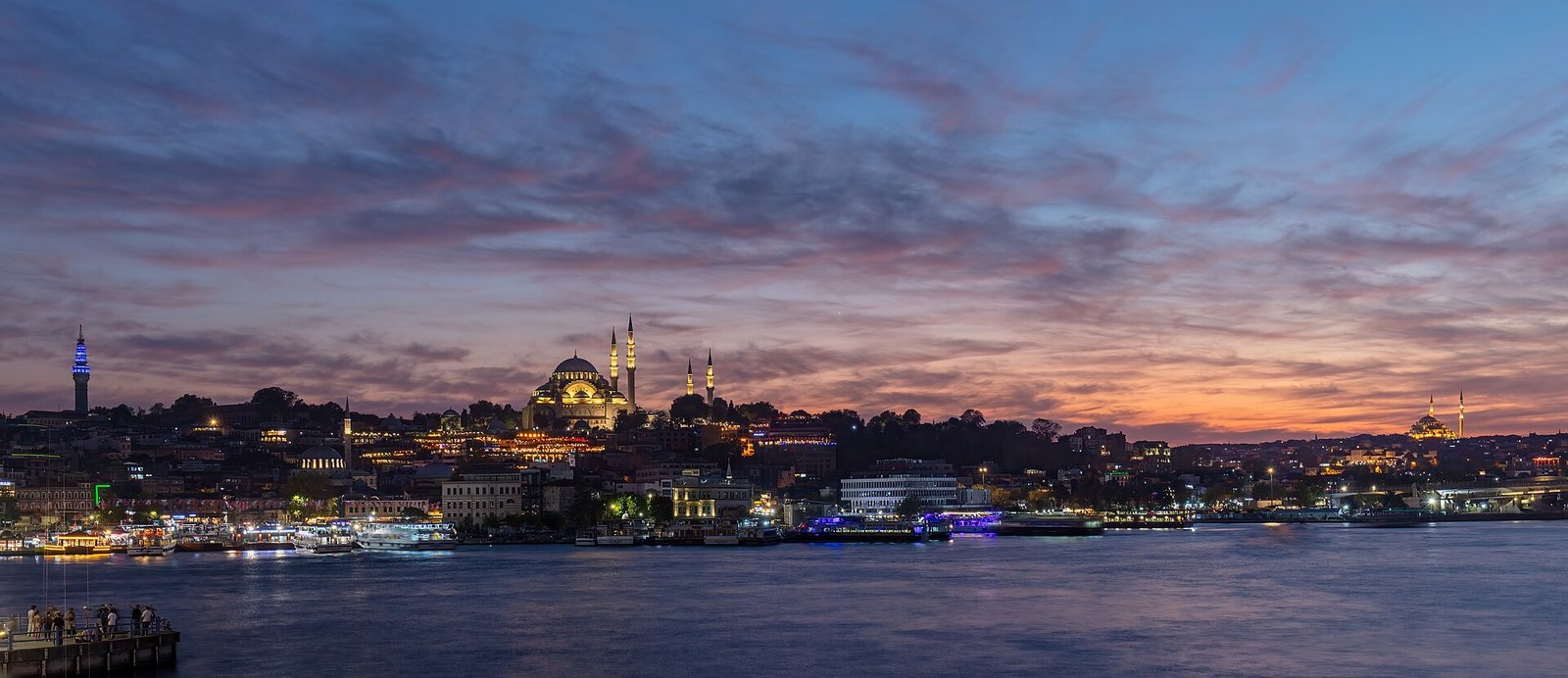 Das Goldene Horn in der Abenddämmerung mit der beleuchteten Süleymaniye-Moschee und Fähren am Ufer